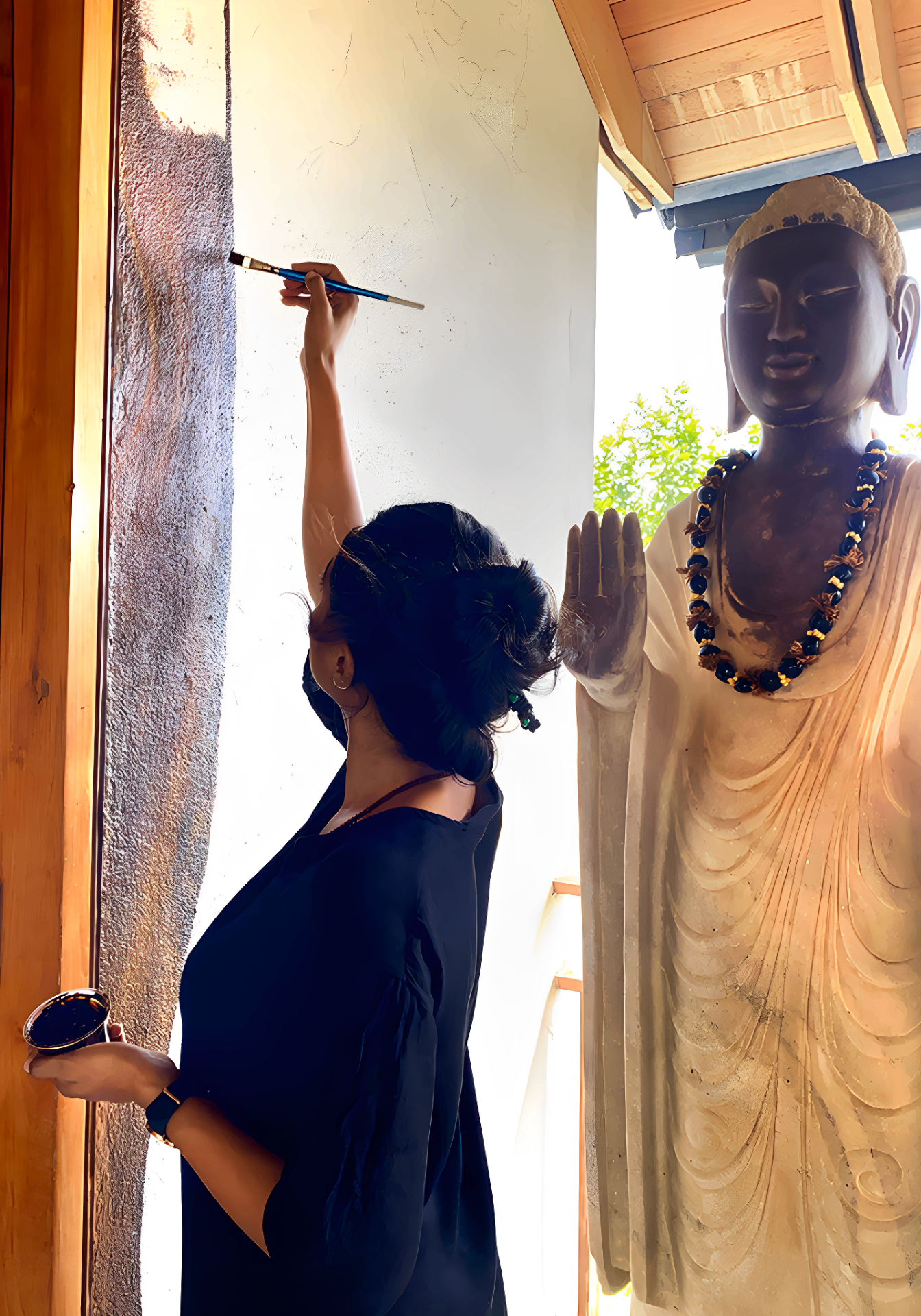Artist painting a textured wall beside a Buddha sculpture