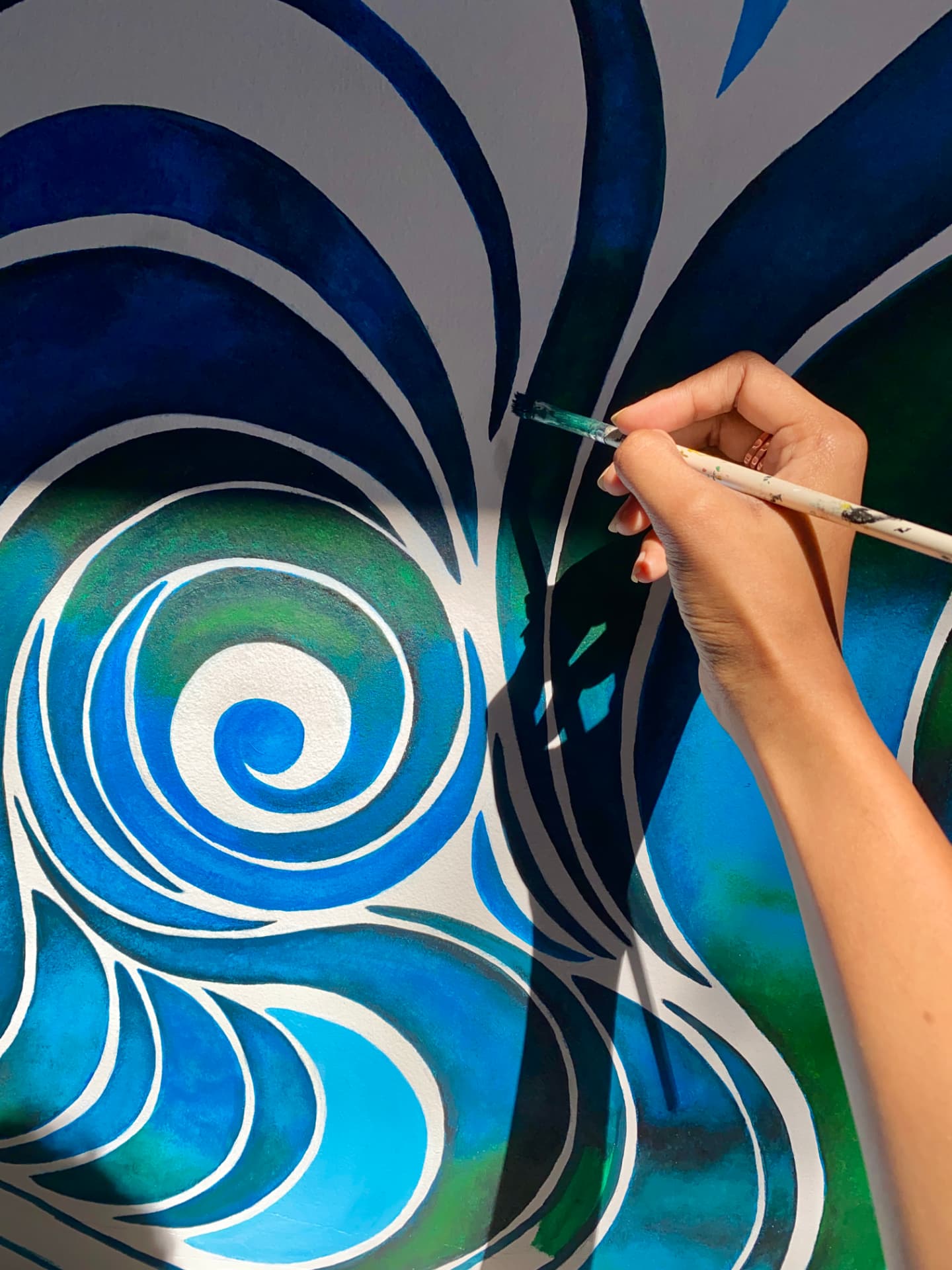 Hand-painted blue and green wave mural being painted on a wall